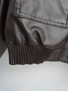 Close-up detail of dark brown faux leather texture and ribbed hem on the jacket