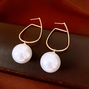 Detailed view of golden geometric line earrings with large white round pearls on textured base