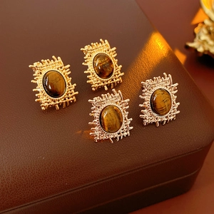 Detail view of square tiger eye stud earrings in gold finish on leather box