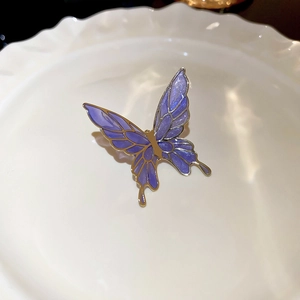 Macro shot of purple butterfly ear clip with gold metal frame on a white plate