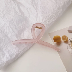 Pince à cheveux mate rose au design torsadé croisé sur un fond esthétique et épuré