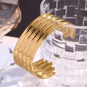 Close-up of golden wide multi-layer striped cuff bracelet on a textured glass background