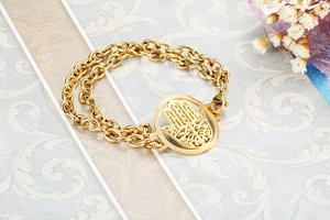 Detailed view of golden double-layer chain bracelet with Hamsa Hand pendant on art paper