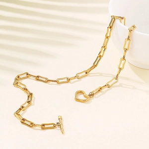 Golden paperclip chain necklace with heart pendant and OT buckle on a minimalist background