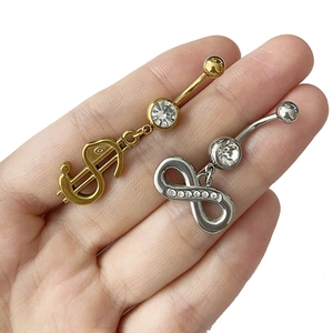 Détail de piercings de nombril en argent et or avec signes dollar et infini sertis de zircons
