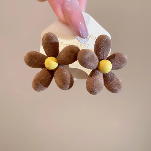 Macro shot of brown flocked flower earrings with velvet texture and yellow center detail