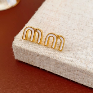 Macro view of gold letter m stud earrings with white enamel finish on texture