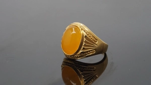 Close-up of golden titanium ring featuring an oval amber gemstone with embossed details