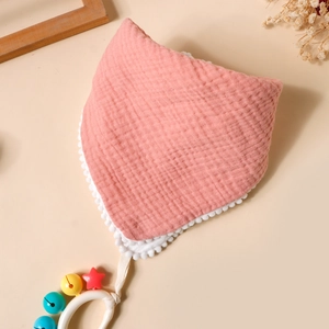 Detailed texture of pink waffle cotton baby bib with pom-pom trim and rattle ring
