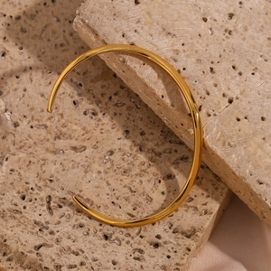 Detail of minimalist wave-shaped gold bracelet on textured natural beige stones