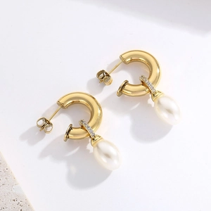 Gros plan de boucles d'oreilles C dorées avec cristaux et perles blanches en goutte