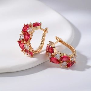 Boucles d'oreilles en or rose avec cristaux rouges et zircons sur une assiette blanche