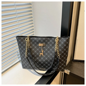 Detail of black tote bag with geometric pattern, chain strap and gold deer pendant