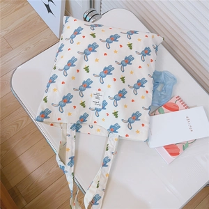 Detail of white cotton tote bag with blue rabbit prints and decorative label on desk