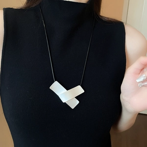 Detail of white geometric layered pendant with black leather cord on a black knit top