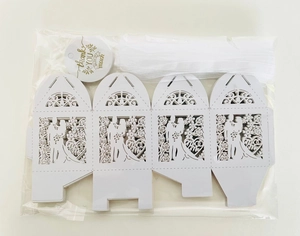 Flat lay of white laser-cut hollow wedding candy box kit with ribbon and thank you tags