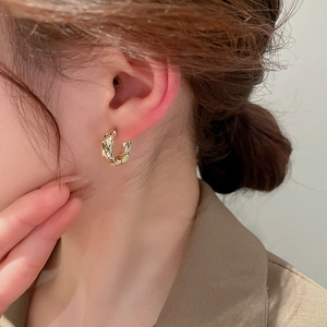 Macro detail of gold-plated hoop earring featuring a unique textured crumpled metal finish
