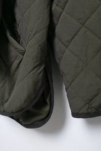 Detail of dark olive green quilted jacket with diamond patterns and ribbed trim cuff