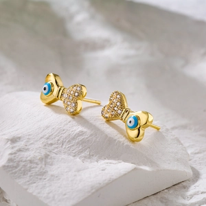 Detail of 18K gold bow stud earring featuring blue evil eye bead and pavé zircon stones
