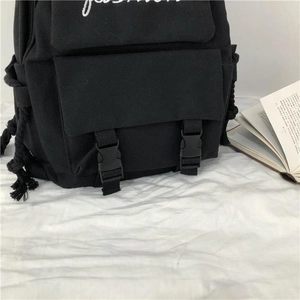 Close-up of black canvas backpack featuring white fashion embroidery and buckle details