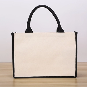 Fashionable beige canvas tote bag with black trim and handles on wooden surface