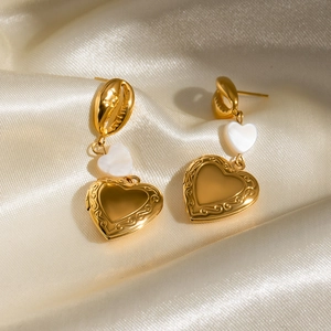 Macro detail of gold-plated shell heart pendant earrings on elegant champagne satin