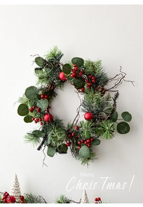 Detail of Christmas wreath with red berries, frosted balls and pine needles on wall