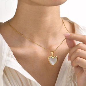 Detail of a heart locket necklace with white shell inlay worn on a white blouse
