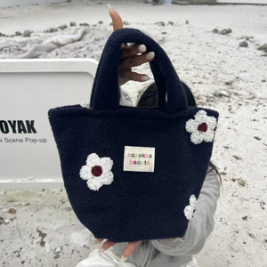 Close-up of small navy blue plush tote bag with white flower patches and brand label