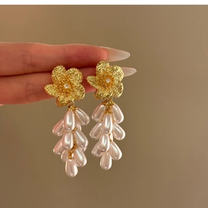 Detail of golden flower drop earrings with pleated petals and cascading white pearls