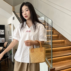 Detail shot of a handmade straw handbag held by a model wearing a white V-neck top
