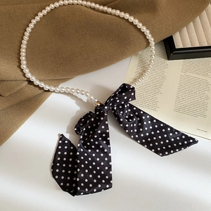 Detail view of pearl necklace with oversized black and white polka dot silk bow