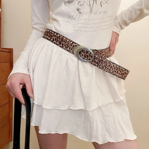 Détail de la ceinture en cuir léopard avec rivets argentés et boucle ovale sur jupe