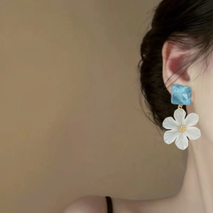 Close-up of white acrylic flower drop earrings with blue square stud on model