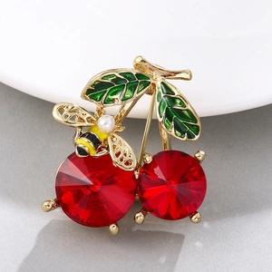 Detail view of cherry brooch with red crystals, green enamel leaves and golden bee pearl
