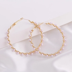 Detail of large gold hoop earrings with wavy design and light pink pearls on white silk