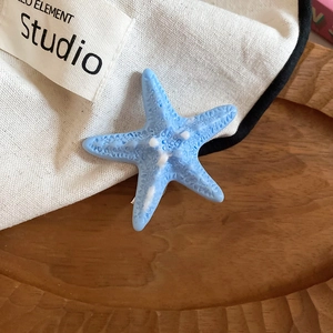 Detailed close-up of a blue starfish hair clip with textured resin on a fabric background