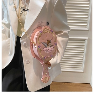 Pink mirror-shaped crossbody bag with angel embroidery and pearl chain on a white blazer