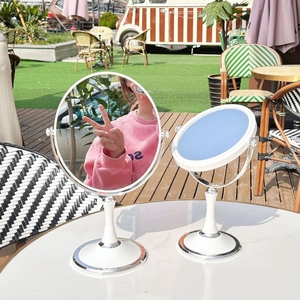 Detail view of round desktop makeup mirror with white stand and metal base outdoors