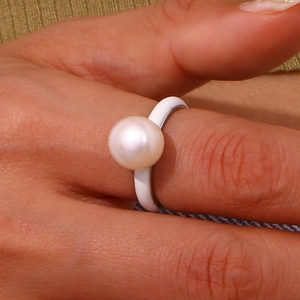 Detail of white enamel ring with single pearl on finger wearing gold knit sleeve