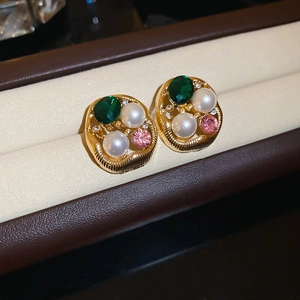Detailed view of vintage gold earrings with green stones and pearls on velvet display