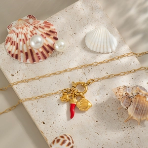 Dettaglio collana oro 18K con ciondolo peperoncino rosso e mare su sfondo di pietra beige