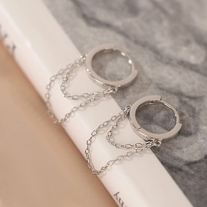 Macro shot of silver dual-layer chain hoop earrings resting on a white book edge