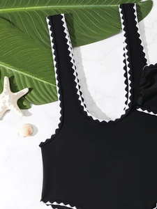 Detailed close-up of black swimwear with white scalloped trim on marble with shells