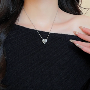 Nahaufnahme eines silbernen Herzanhängers mit Kreuz an einer Kette an einem Model