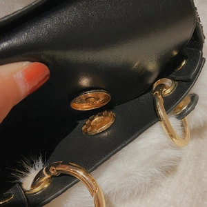 Detail of gold magnetic snap closure on black leather and white faux fur handbag