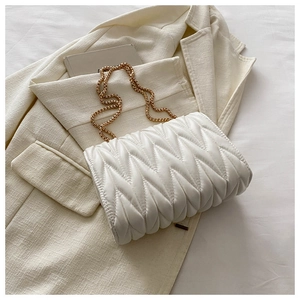 Detail of white quilted crossbody bag with golden chain strap on a blazer background
