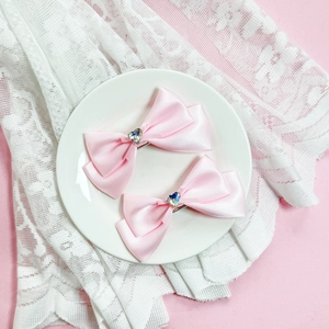 Détail de barrettes à nœuds en satin rose avec cristal en forme de cœur sur dentelle blanche