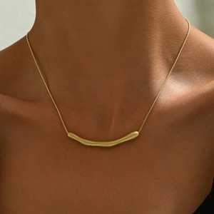 Collana minimalista dorata con un ciondolo curvo opaco su una sottile catena a serpente