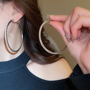 Close-up of oversized silver hoop earrings with shimmering crystals on model and hand